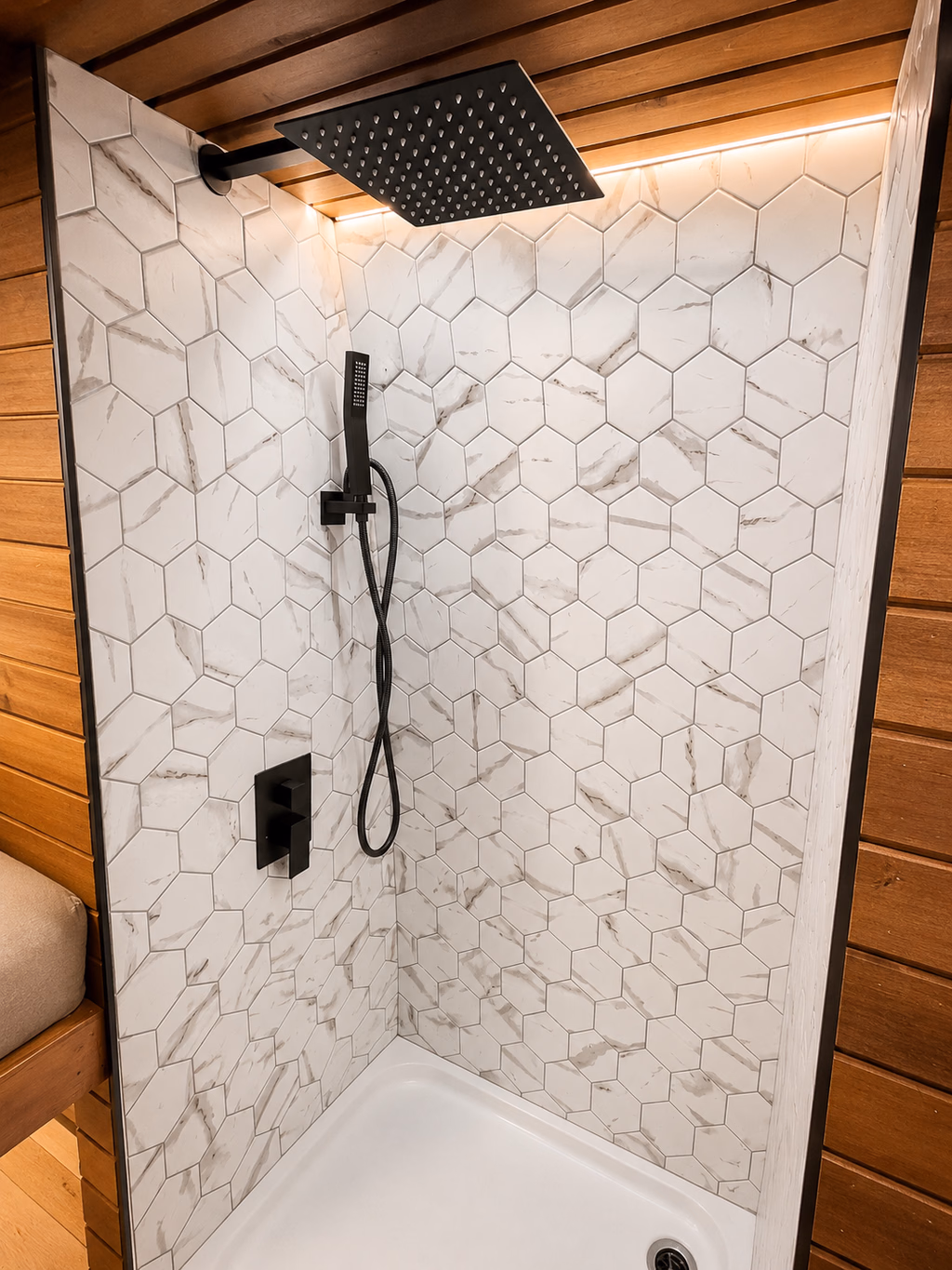 Douche finie avec robinetterie noire, céramique hexagonale et plafond en bois.